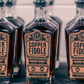 A group of Copper Fiddle Bourbon Whiskey bottles placed side by side on a table.