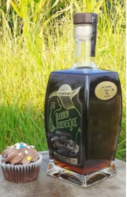 A bottle of Rubenesque on a stone tablet outdoors with a chocolate cupcake beside it.