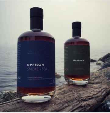 A shot of two bottles of  Oppidan Smoke + Sea Bourbon on the shoreline.