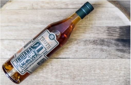 A Truth Hills Indiana Straight Rye Whiskey bottle is laid on a wooden table.