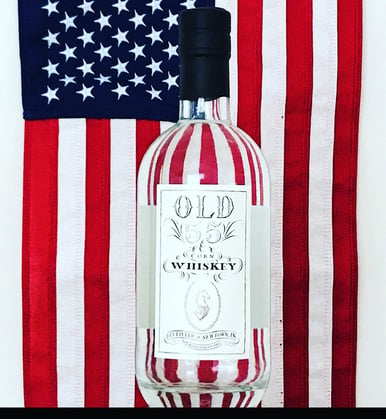 A bottle of Old 55 Corn Whiskey standing in front of an American flag backdrop.