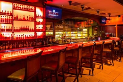 Cocktail counter with empty chairs, full shelves, and two TVs mounted above the counter with the text “blend” flashing