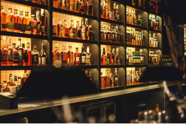 Seven Grand Denver’s whiskey bar. The shelves are lit up and filled with liquor bottles behind the counter.