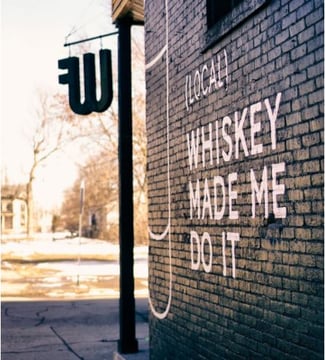 West Fork Whiskey’s brick wall facade with the text (local) whiskey made me do it painted on it.