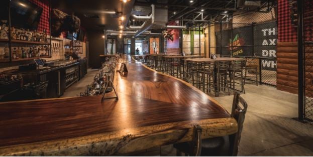 A counter built out of wood with empty chairs in front and with a group of empty chairs and tables on the right side.