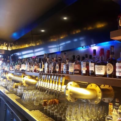 Whiskey bar with empty wine and whiskey glasses below the shelf and an entire shelf on top with liquor bottles.